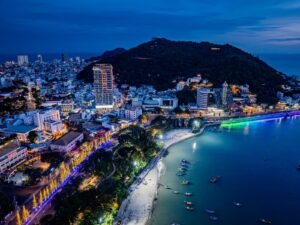 Stunning aerial view of a lively coastal city at night, illuminated by vibrant lights.