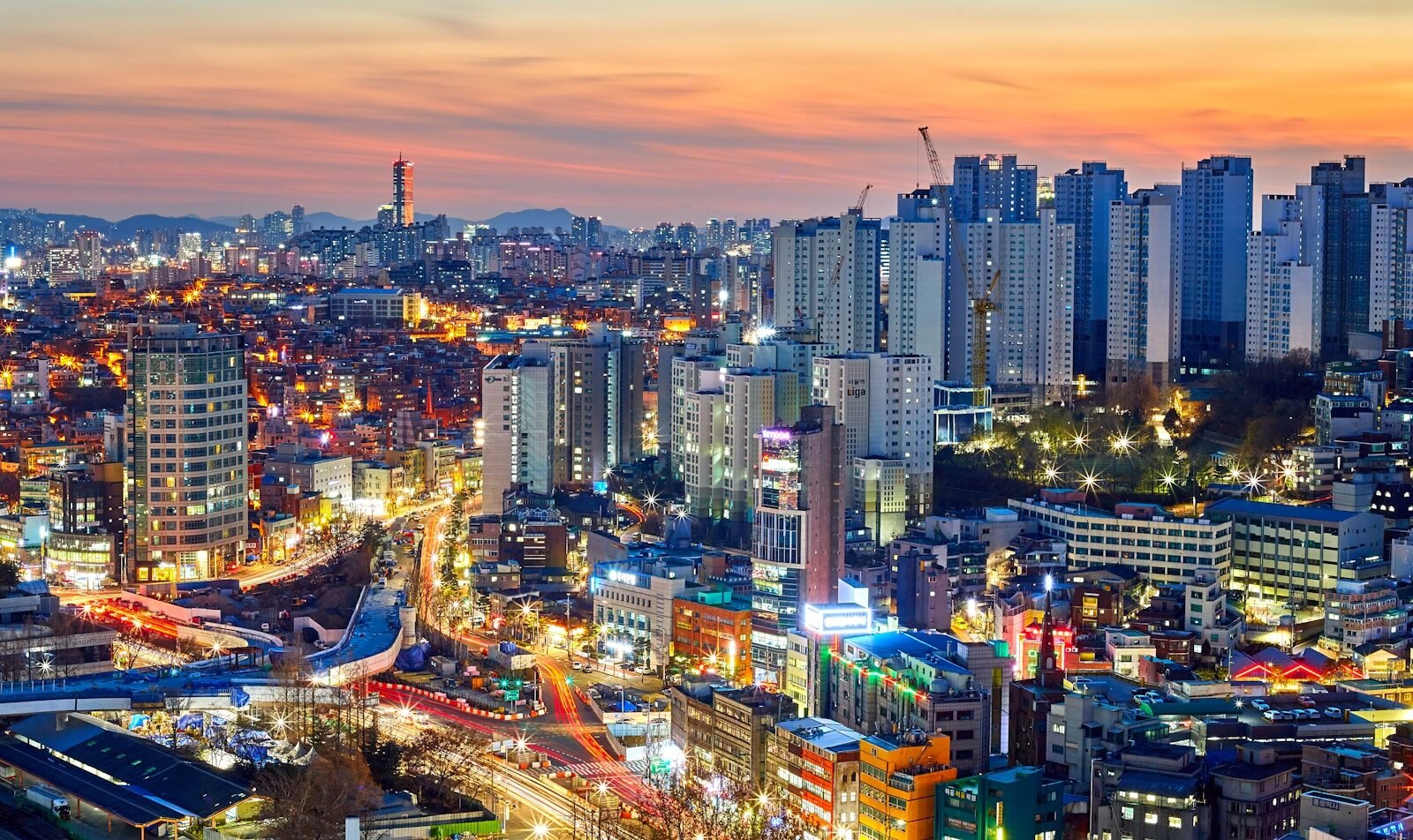 A dense cityscape in Seoul, South Korea, under a warm orange sky at night
